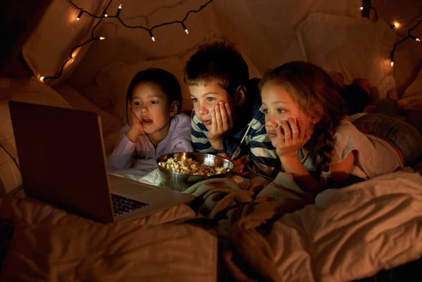 枕は爆弾のためだ。3人の子供が毛布の中でノートパソコンを使って - 写真・画像