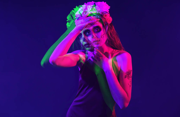Young woman with painted skull on her face for Mexico's Day of the Dead (El Dia de Muertos) against dark blue background  - Photo, Image