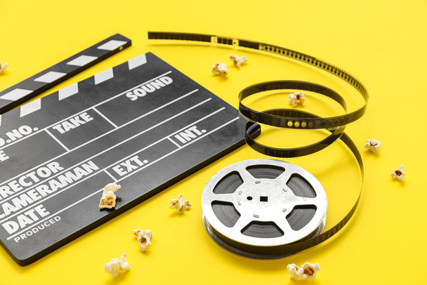 Movie clapper with reel and popcorn on yellow background - Photo, Image