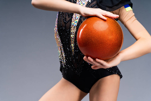 Close-up. The body of a little girl gymnast in an elegant costume of a winner for performances and a gymnastic ball in her hands. High quality photo - Foto, Bild