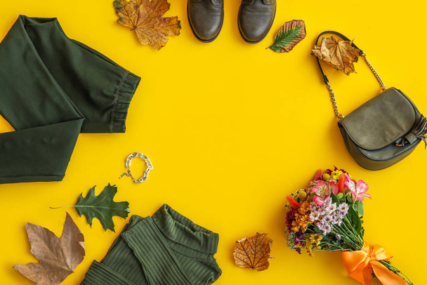 Marco hecho de ropa elegante, zapatos, accesorios, flores y hojas de otoño sobre fondo amarillo - Foto, imagen