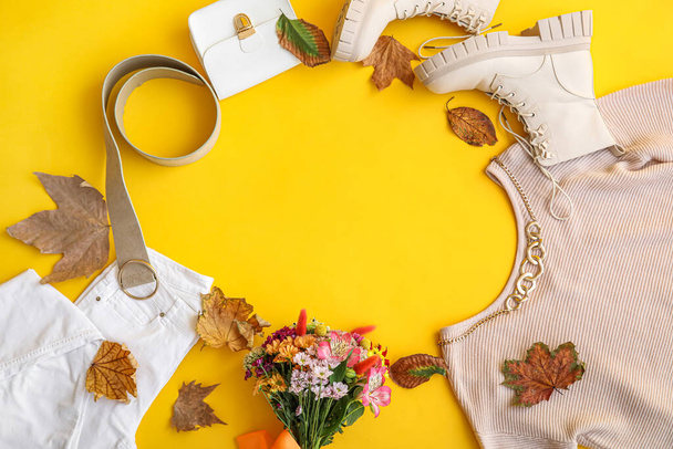 Cadre fait de vêtements élégants, bottes, accessoires, fleurs et feuilles d'automne sur fond jaune - Photo, image