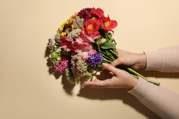 Manos femeninas y ramo de hermosas flores sobre fondo beige - Foto, Imagen