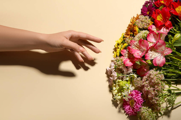 Γυναικείο χέρι και μπουκέτο από όμορφα λουλούδια σε μπεζ φόντο - Φωτογραφία, εικόνα