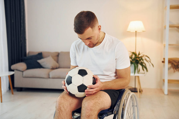 With soccer ball. Disabled man in wheelchair is at home. - Photo, image