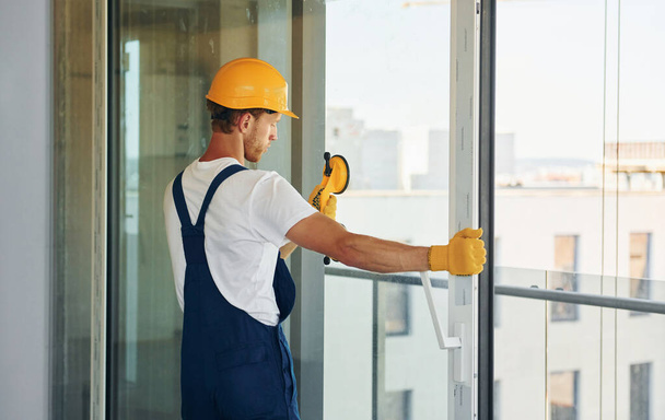 Clearing windows. Young man working in uniform at construction at daytime. - 写真・画像