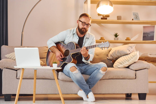 Cozy atmosphere. Man in casual clothes and with acoustic guitar is indoors. - Photo, Image