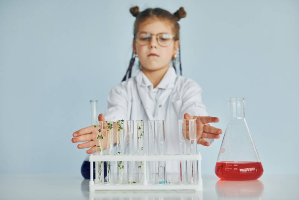 Works with test tubes. Little girl in coat playing a scientist in lab by using equipment. - Foto, Imagen