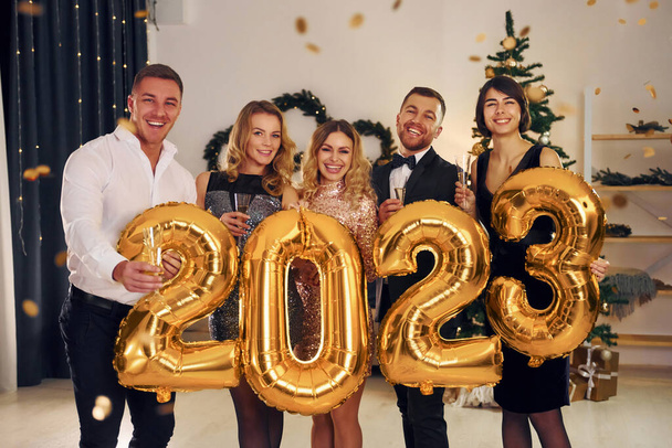 Holding balloons with 2023 number. Group of people have a new year party indoors together. - Photo, image