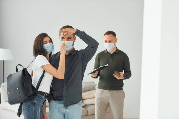 Man helps the young couple in choosing an apartment. In masks. - Photo, image