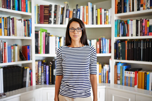 Kitaplarla çevrili olmak bir ayrıcalıktır. Çekici bir genç kadın kütüphanesinde duruyor. - Fotoğraf, Görsel