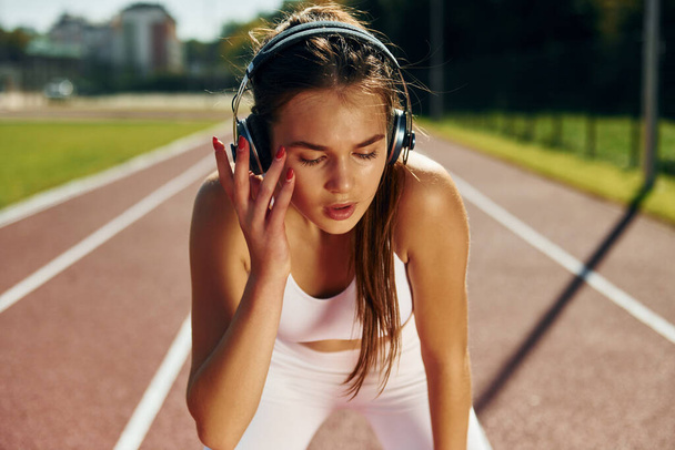 Listening to the music in headphones. Young woman in sportive clothes is exercising outdoors. - Фото, изображение