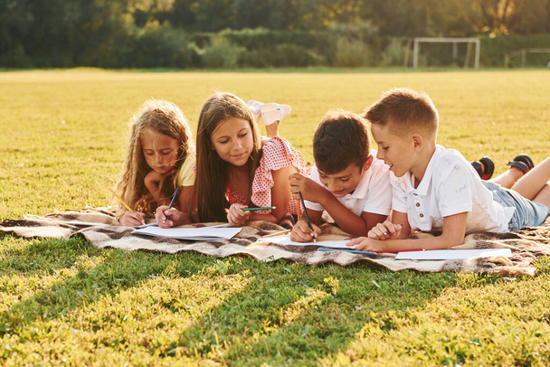 Drawing pictures. Group of happy kids is outdoors on the sportive field at daytime. - Φωτογραφία, εικόνα