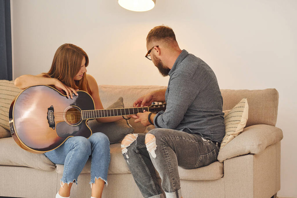 Guitar teacher showing how to play the instrument to young woman. - Foto, afbeelding