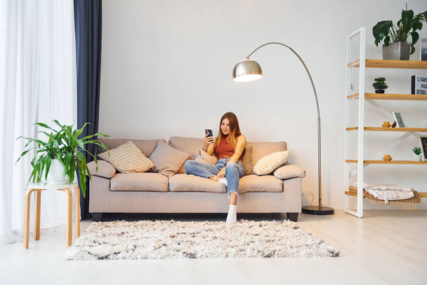 Young woman is sitting on the sofa in domestic room. - Foto, Bild