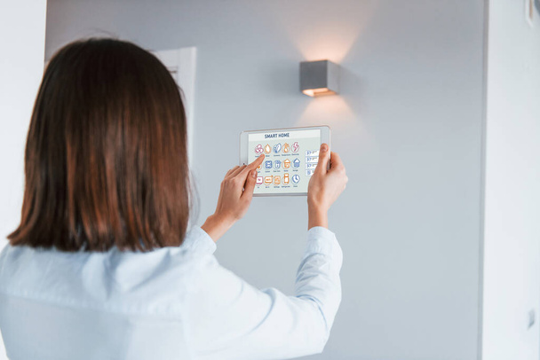 Rear view of woman that is indoors controlling smart home technology. - Photo, image