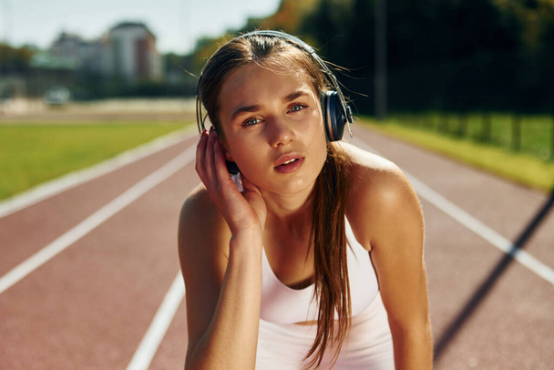 Listening to the music in headphones. Young woman in sportive clothes is exercising outdoors. - Foto, Imagem
