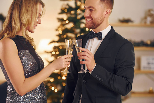 Cheering with glasses of alcohol. Happy couple have a new year party indoors together. - Фото, зображення