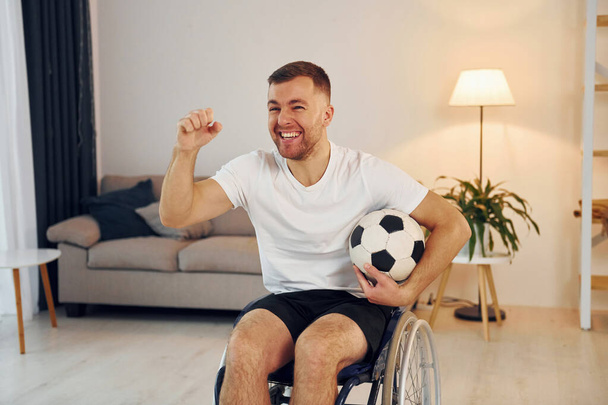 Soccer fan with ball. Disabled man in wheelchair is at home. - Valokuva, kuva