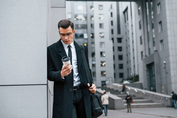 Standing near the building. Businessman in black suit and tie is outdoors in the city. - Foto, Imagen