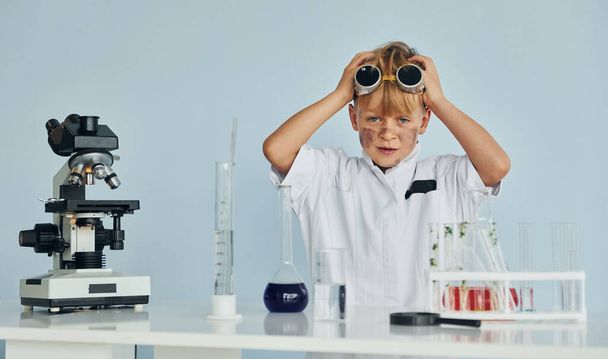 Scared little boy in coat playing a scientist in lab by using equipment. - Фото, зображення
