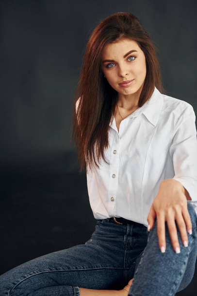 In white shirt and blue jeans. Young beautiful woman is posing for the camera in the studio. - 写真・画像