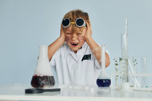 Scared little boy in coat playing a scientist in lab by using equipment. - 写真・画像