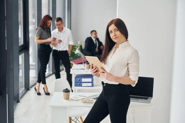 Woman holds tablet. Group of people in official formal clothes that is indoors in the office. - Fotoğraf, Görsel