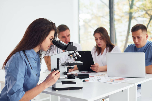 Unter dem Mikroskop. Gruppe junger Ärzte arbeitet in moderner Praxis zusammen. - Foto, Bild