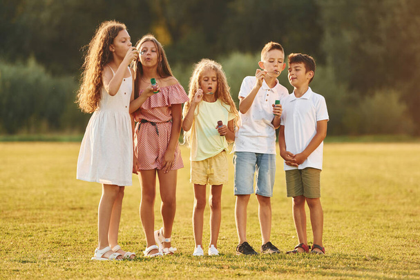 Beautiful sunlight. Group of happy kids is outdoors on the sportive field at daytime. - Foto, afbeelding