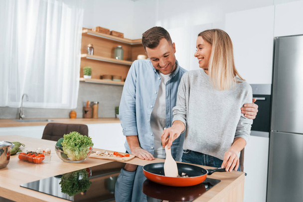 Frying food in a pan. Couple preparing food at home on the modern kitchen. - Фото, изображение