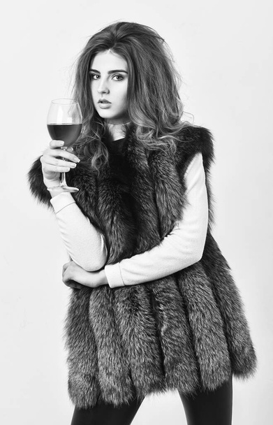 Luxury winery concept. Fashion model long hair fur coat or vest hold wineglass. Fashionable lady likes luxury. Girl enjoy luxury lifestyle attributes. Woman drink wine wear luxury fur clothing. - Φωτογραφία, εικόνα