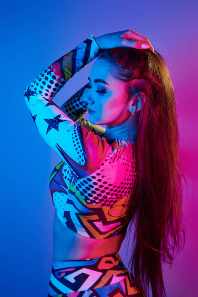 Confident woman in colorful clothes standing in the studio with neon light. - Foto, imagen