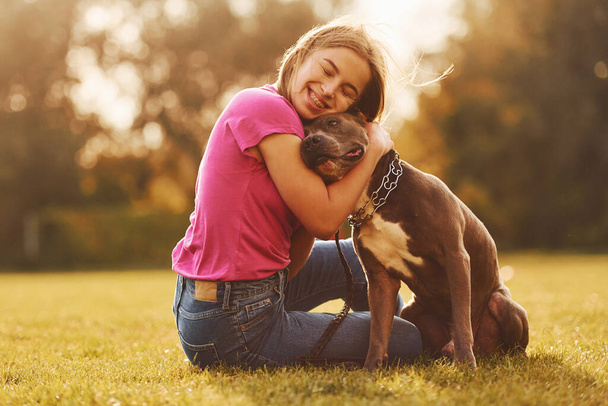 Embracing the dog. Woman in casual clothes is with pit bull outdoors. - Zdjęcie, obraz