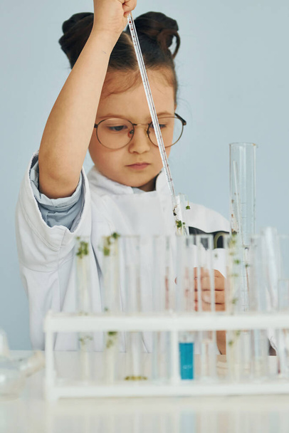 Workes with liquid that is in test tubes. Little girl in coat playing a scientist in lab by using equipment. - Фото, зображення