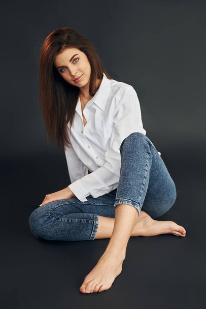 Sits on the floor. Young beautiful woman is posing for the camera in the studio. - Photo, image