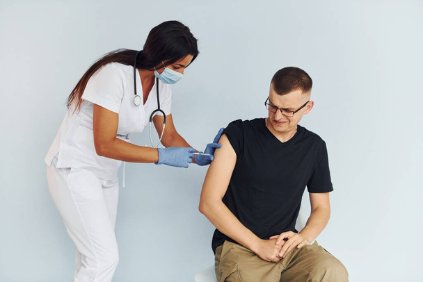 Man is nervous. Doctor in uniform making vaccination to the patient. - Foto, Bild