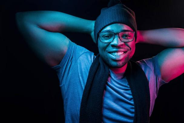 In hat and scarf. Futuristic neon lighting. Young african american man in the studio. - Φωτογραφία, εικόνα