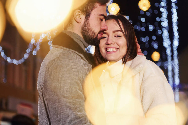 Beautiful garland lighting. Happy young couple celebrating New year outdoors on the street. - Φωτογραφία, εικόνα