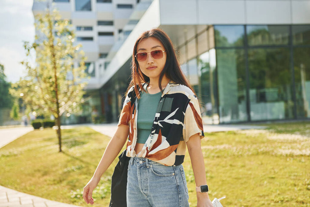In sunglasses. Young asian woman is outdoors at daytime. - Фото, зображення