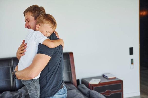 Embracing each other. Father and son is indoors at home together. - Foto, immagini