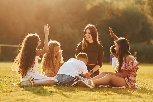 With woman. Group of happy kids is outdoors on the sportive field at daytime. - Photo, Image