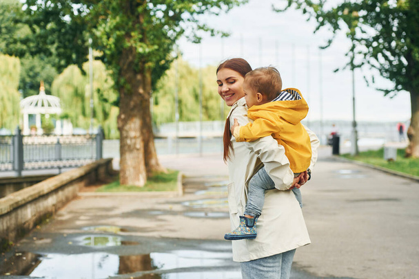Junge liegt auf den Schultern. Mutter geht nach dem Regen mit ihrem Sohn im Park spazieren. - Foto, Bild