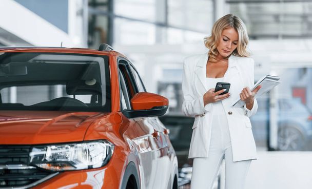 Holding phone. Woman in formal clothes is indoors in the autosalon. - Foto, Imagem