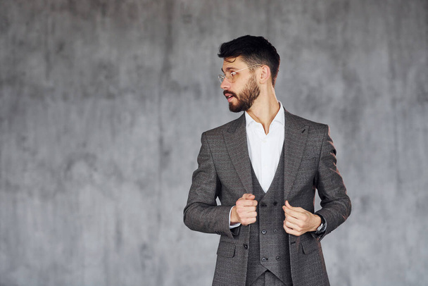 Standing against grey background. Young stylish businessman in suit indoors. Conception of success. - Foto, Imagen
