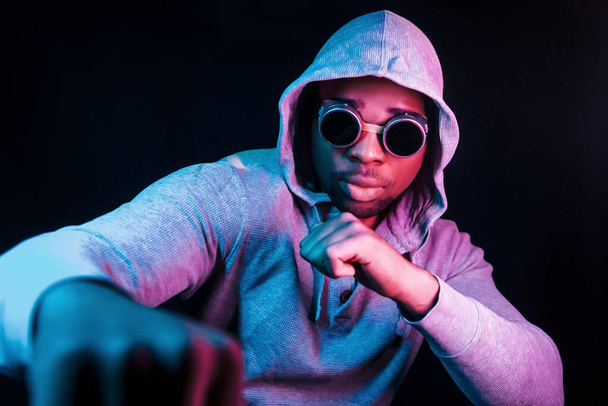 Cyberpunk style glasses. Futuristic neon lighting. Young african american man in the studio. - Фото, изображение