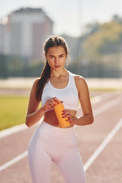 Holding bottle of watter. Young woman in sportive clothes is exercising outdoors. - Foto, Bild
