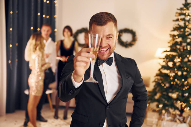 Man with glass of champagne is cheering. Group of people have a new year party indoors together. - Φωτογραφία, εικόνα