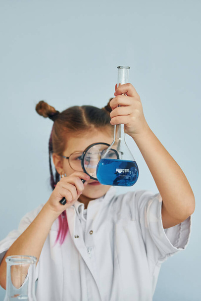 Holds magnifying glass. Little girl in coat playing a scientist in lab by using equipment. - Fotó, kép
