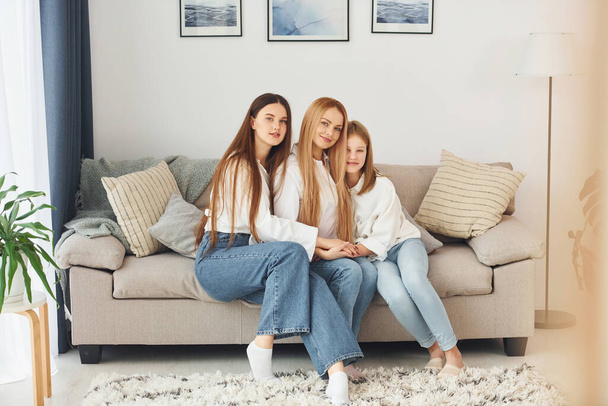 Sitting on the sofa. Young mother with her two daughters at home at daytime. - Fotoğraf, Görsel